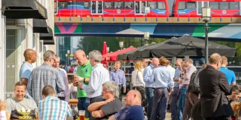 People enjoying drinks at a Seattle brewery neighborhood with a city transit bus overhead.