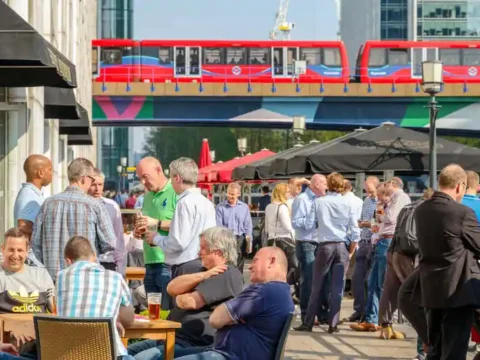 The Walkable Brewery Neighborhood: What It Costs to Live Near Seattle’s Taproom Clusters People enjoying drinks at a Seattle brewery neighborhood with a city transit bus overhead.