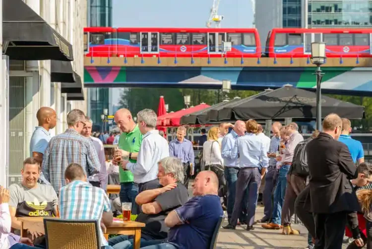 People enjoying drinks at a Seattle brewery neighborhood with a city transit bus overhead.