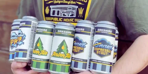 Oakshire Brewing Ceasing Operations, Ending a 20-Year Run a person holding an armful of brightly colored beer cans