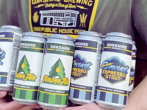 Oakshire Brewing Ceasing Operations, Ending a 20-Year Run a person holding an armful of brightly colored beer cans