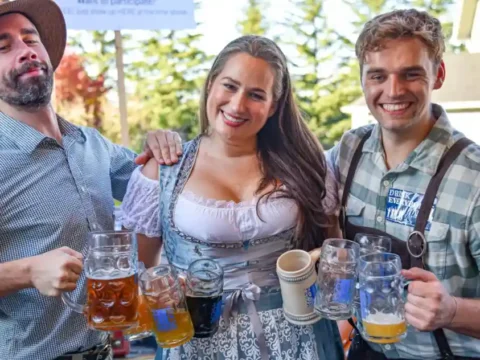 This Weekend, Join Ounces Taproom for Three Days of Oktoberfest Fun Three people in Oktoberfest garb with mugs of beer