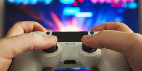 Why Some Games Stay Popular For Decades While Others Disappear Person playing a video game with a controller in front of a colorful gaming screen
