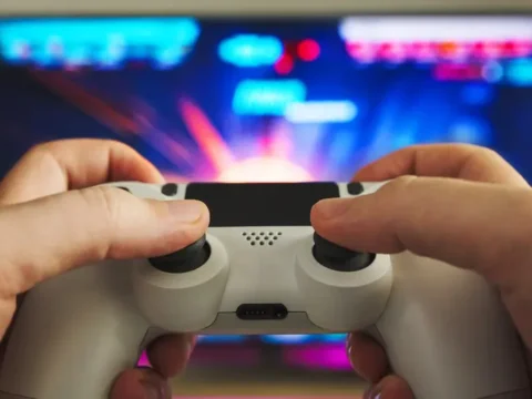 Why Some Games Stay Popular For Decades While Others Disappear Person playing a video game with a controller in front of a colorful gaming screen