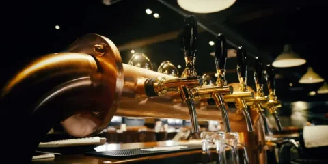 Beer draft taps with black handles lined up at a dimly lit bar