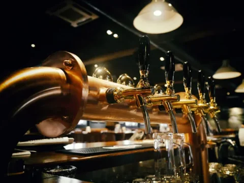 Beer draft taps with black handles lined up at a dimly lit bar