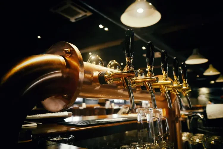 Beer draft taps with black handles lined up at a dimly lit bar