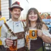 The Weekend’s Beer Events – October 2nd Through 4th, 2026 two people in Oktoberfest garb hoisting mugs of beer