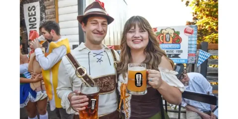 two people in Oktoberfest garb hoisting mugs of beer