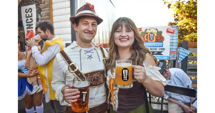 The Weekend’s Beer Events – October 2nd Through 4th, 2026 two people in Oktoberfest garb hoisting mugs of beer